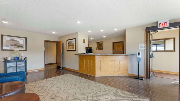 A reception area with a wooden counter, a blue sofa, a patterned rug, and an exit sign. - Comfort Inn Lexington (Lexington)
