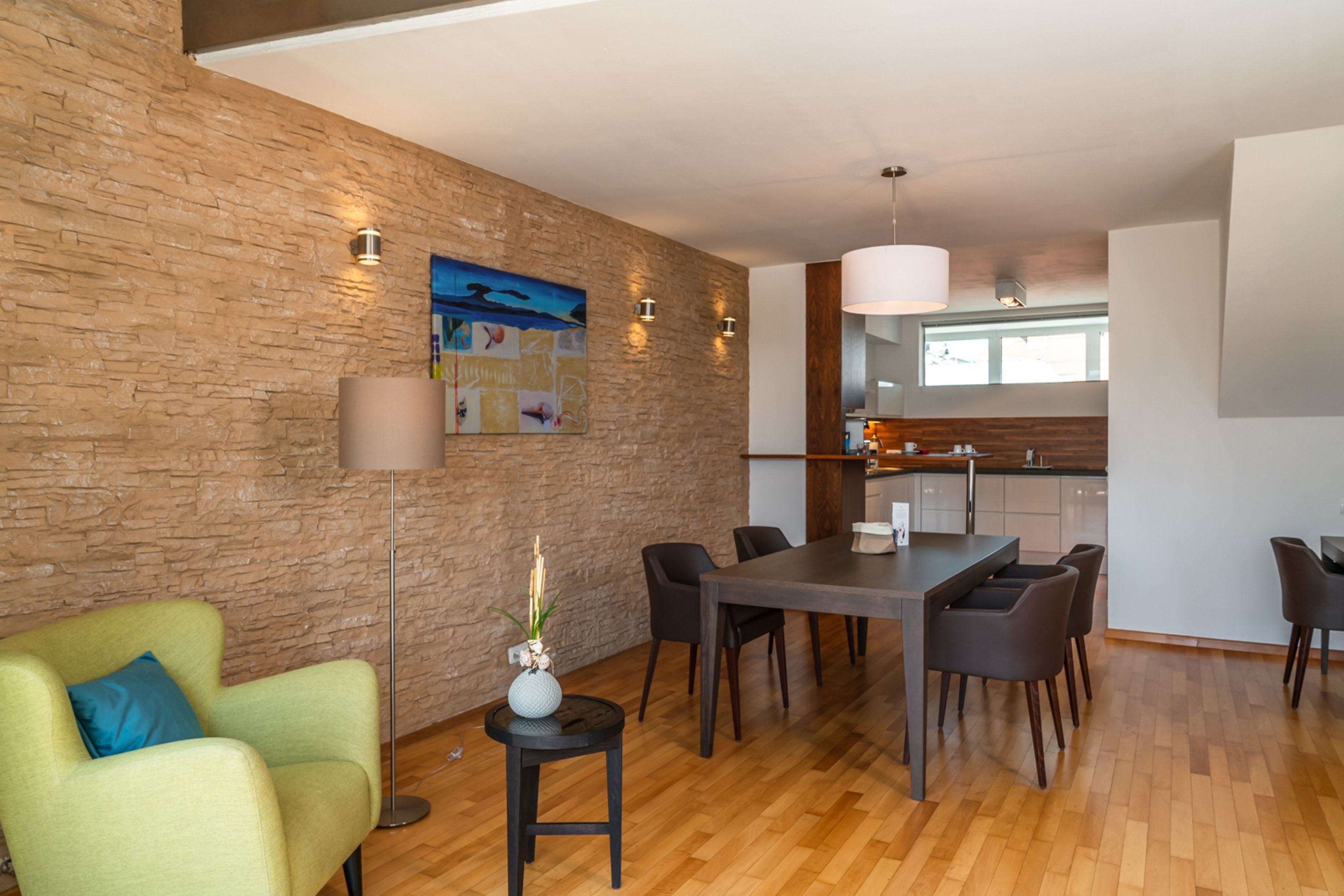 A modern kitchen with a stone wall, wooden flooring, and a dining area with a table and chairs.
