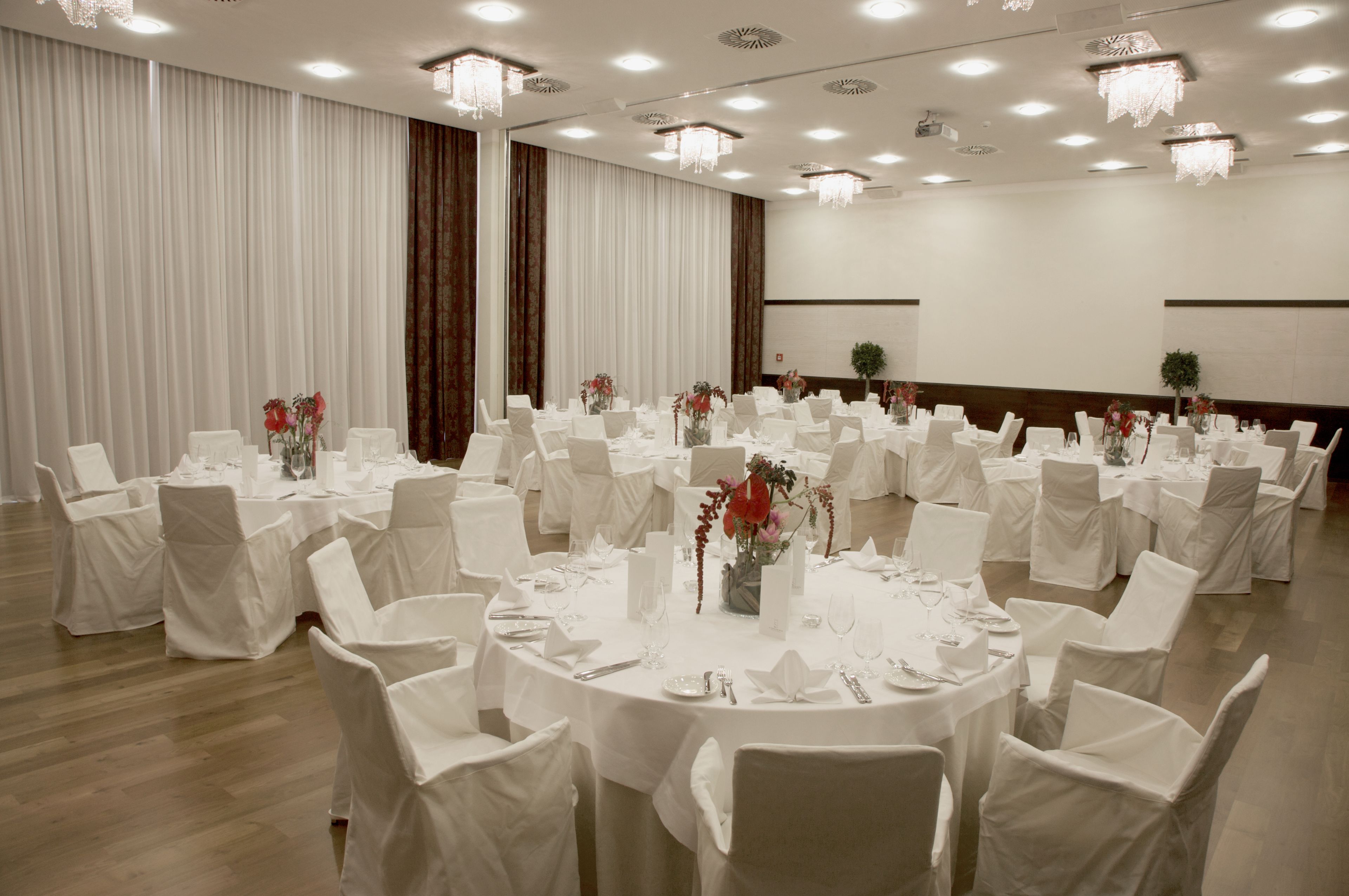 Een balzaal met ronde tafels voor diners, witte stoelen en kroonluchters.