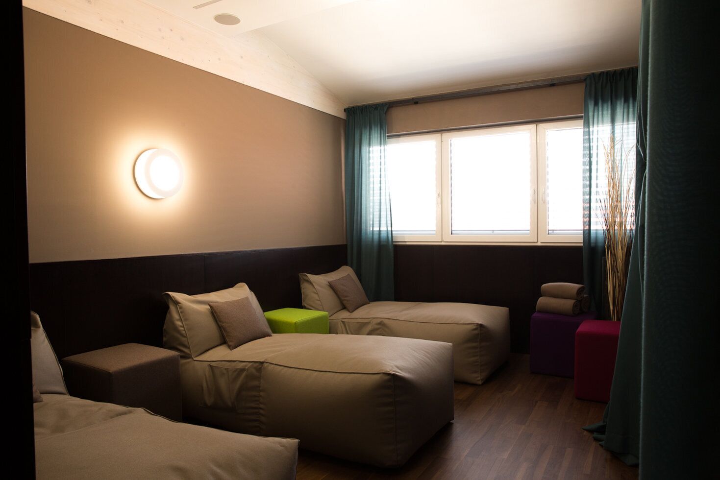 Habitación de hotel con cama, dos sofás, un taburete verde y una ventana con cortinas.