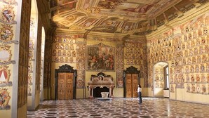 An ornate hall with a tiled floor, a large mural, and numerous coats of arms on the walls.