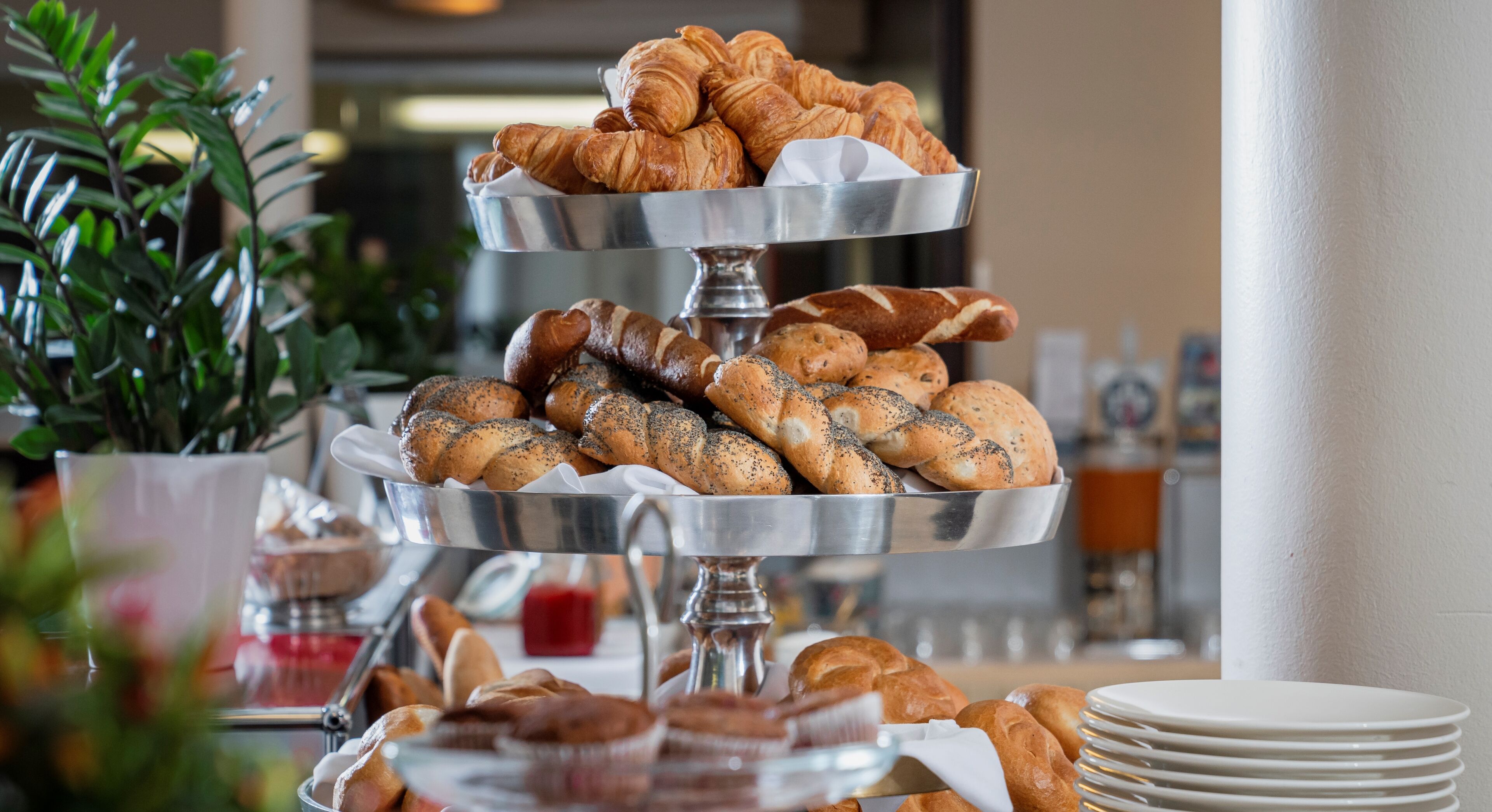 A buffet with various baked goods, including croissants and bread rolls, arranged on a metal stand.