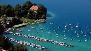 An aerial view of a marina with numerous boats docked, surrounded by lush greenery and a few buildings.