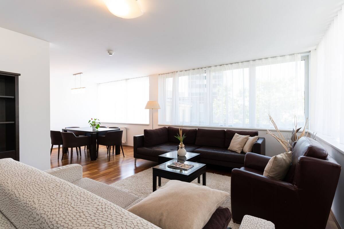 A modern living room with a sofa, coffee table, and a dining area with chairs and a table.
