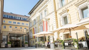 A hotel with a glass entrance, outdoor seating with umbrellas, and a sign reading "HOTEL".