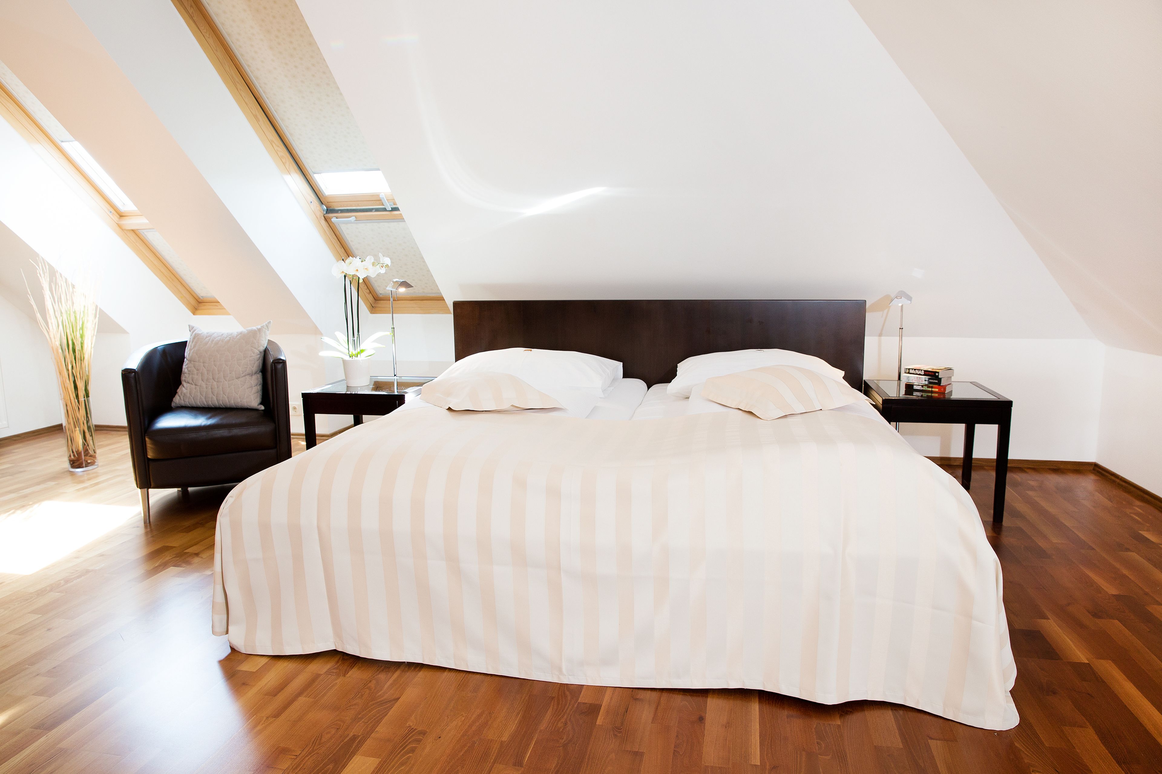 Une chambre avec un grand lit, une table de chevet, une chaise et une plante en pot.