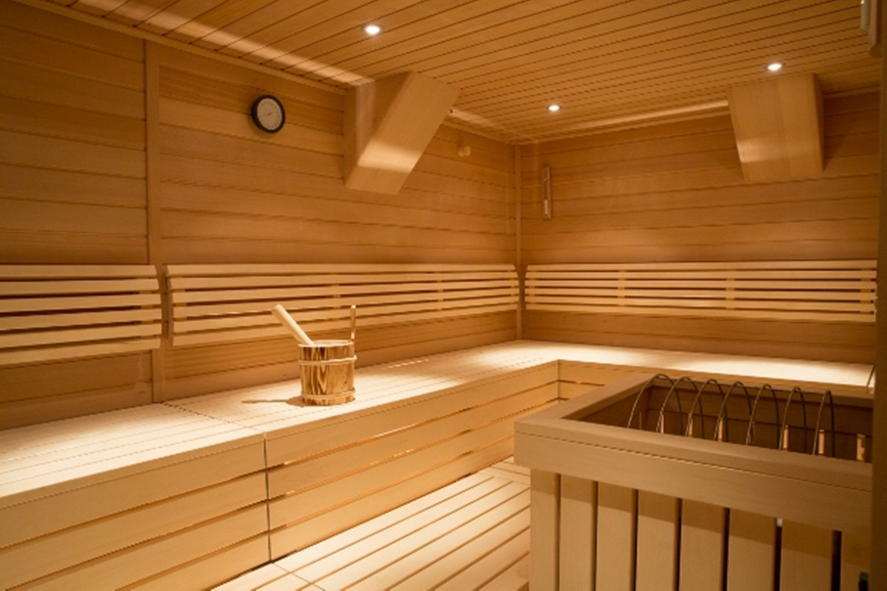 Eine Holzsauna mit Bänken, einer Uhr und einem Holzeimer.
