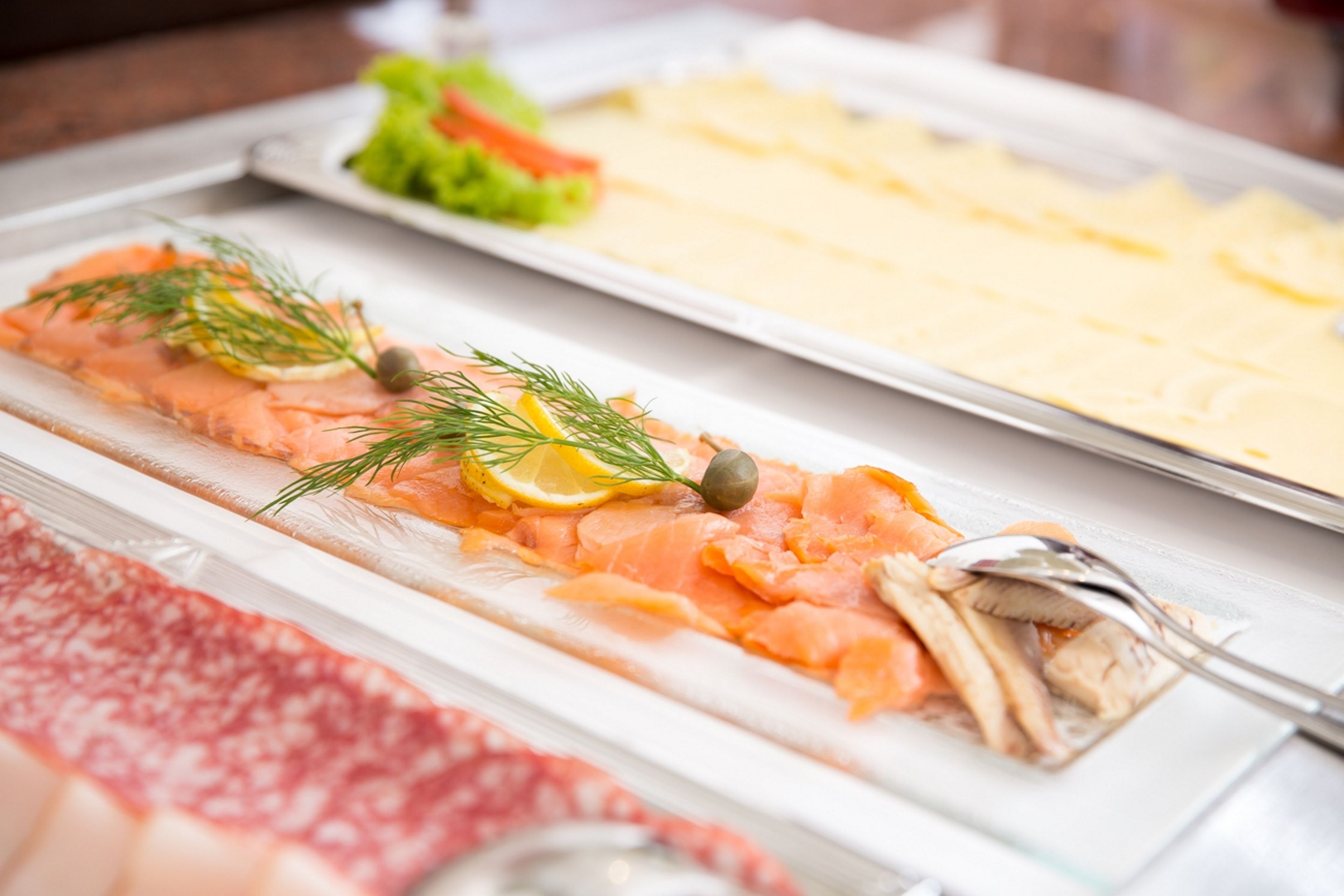 A buffet with salmon, cheese, and a salad.