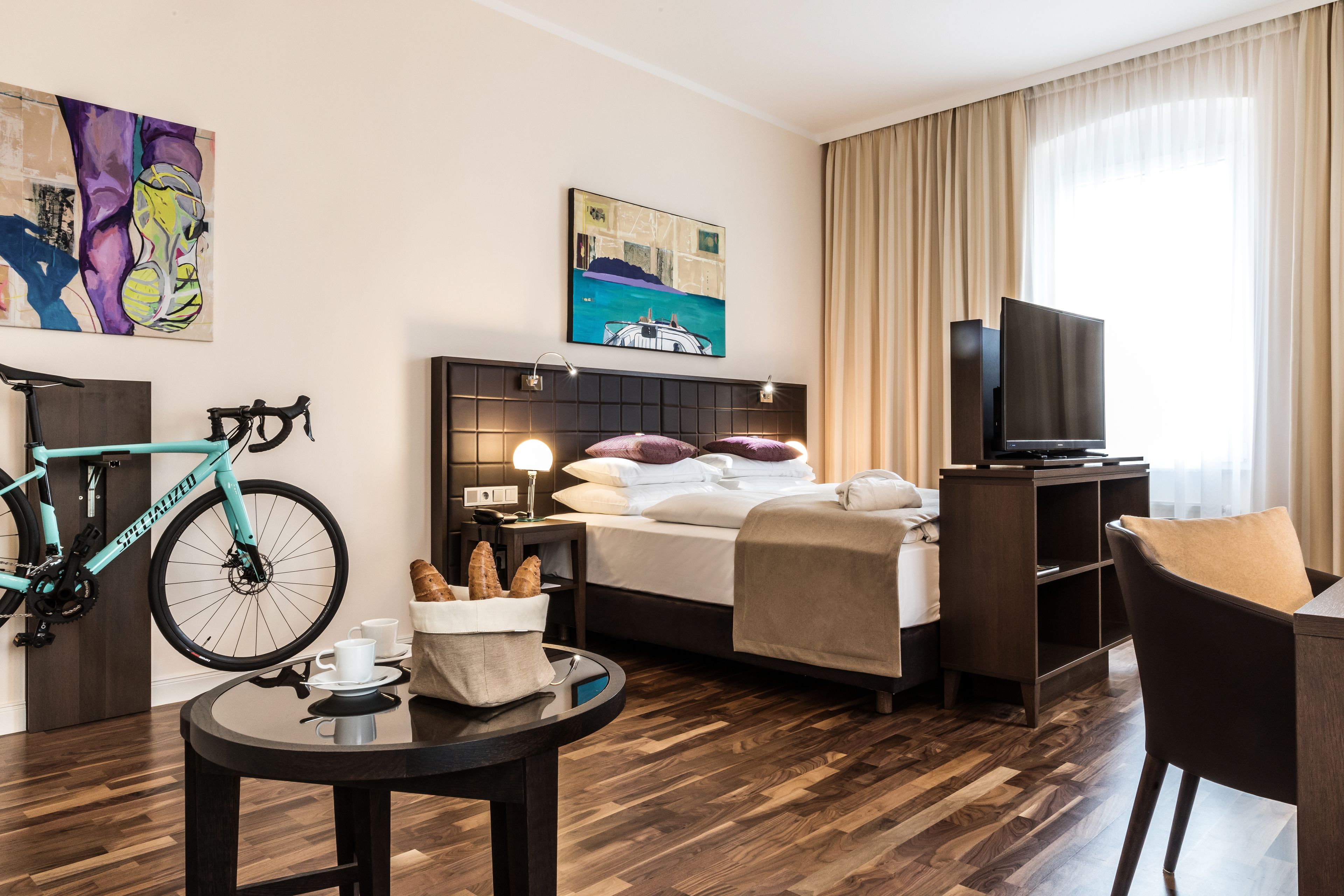 Ein Hotelzimmer mit einem Bett, einem Fernseher, einem Fahrrad und einem Essbereich mit Tisch und Stühlen.