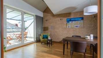 A modern dining area with a wooden table and chairs, a green armchair, and a large window with a view of the outside.