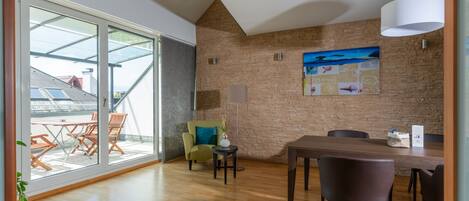 A modern dining area with a wooden table and chairs, a green armchair, and a large window with a view of the outside.