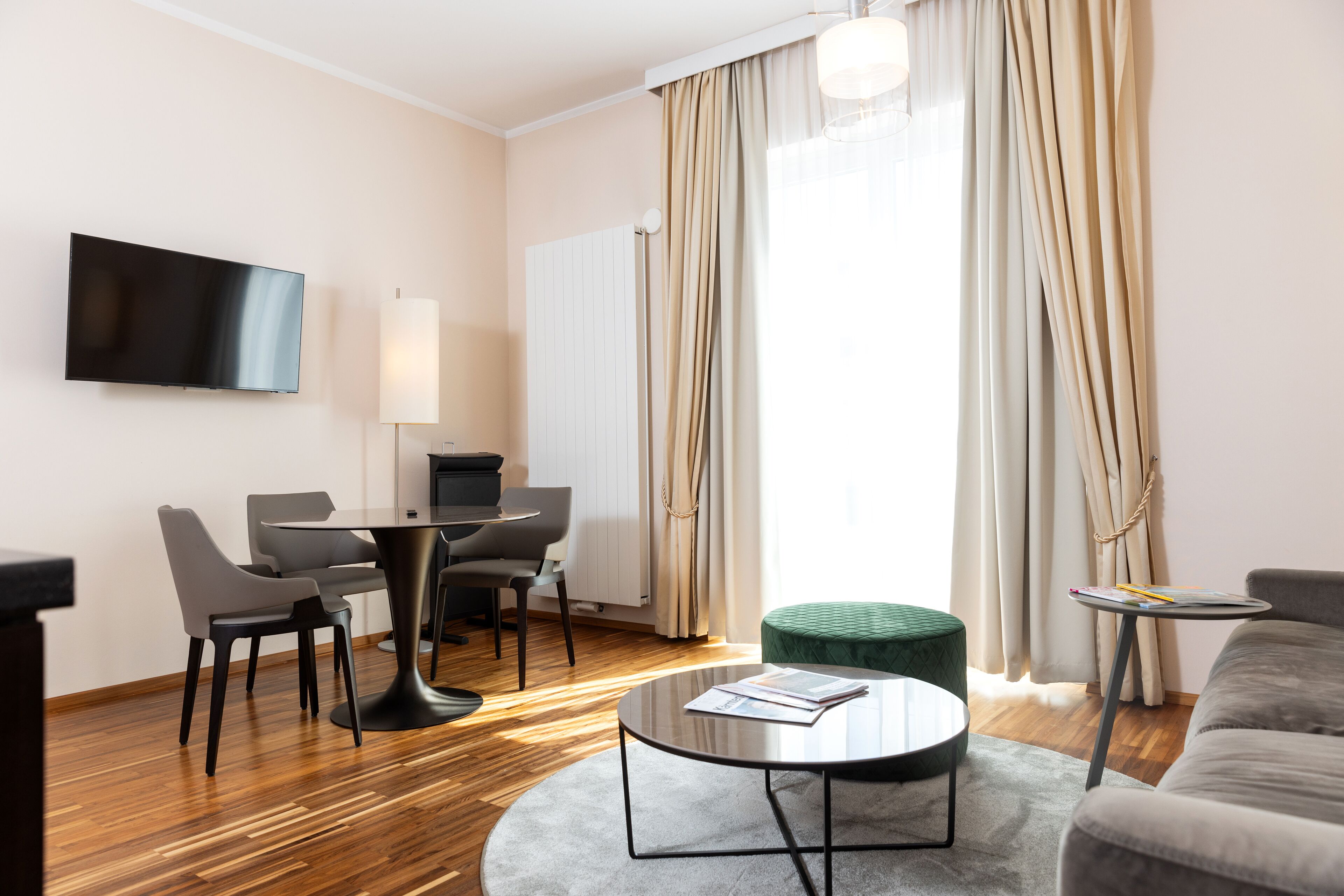 Una habitación de hotel moderna con televisión de pantalla plana, un área de comedor con sillas y una mesa, un sofá y una pequeña mesita auxiliar.
