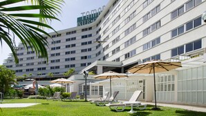 A hotel with a modern design, featuring a large building with multiple floors and a prominent sign. There are outdoor seating areas with umbrellas and lounge chairs. - Hotel Tamanaco Caracas (Caracas)