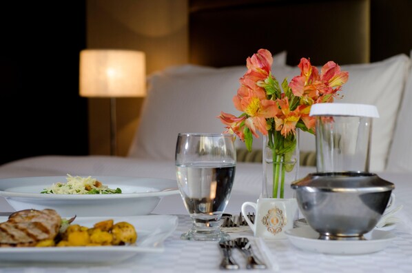 A neatly arranged breakfast table with plates of food, a glass of water, a vase of flowers, and a tea set.
