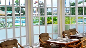 A dining area with tables and chairs, large windows with a view of a pool and greenery. - Hotel Tamanaco Caracas (Caracas)