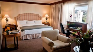 A hotel room with a bed, two bedside tables, a chair, a desk, and a view of buildings. - Hotel Tamanaco Caracas (Caracas)
