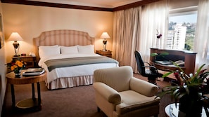 A hotel room with a bed, two bedside tables, a chair, a desk, and a view of buildings. - Hotel Tamanaco Caracas (Caracas)