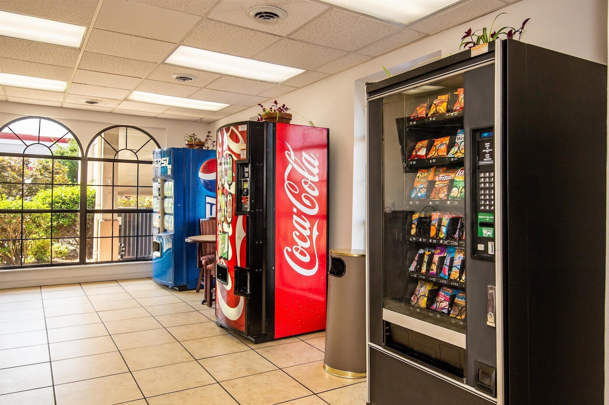 A vending area with Coca-Cola and Pepsi machines, a trash bin, and a window with a view of greenery.