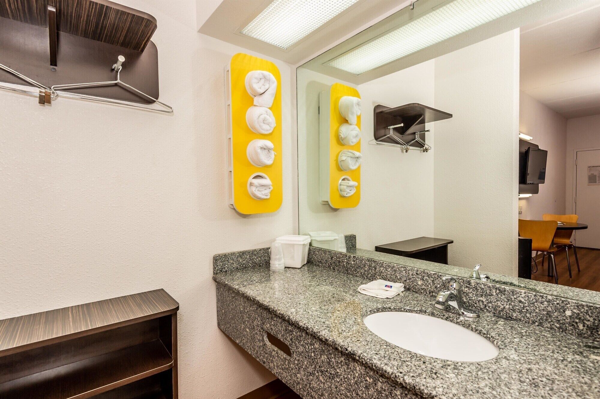 A hotel bathroom with a granite sink, a mirror, a towel rack, and a shower area.
