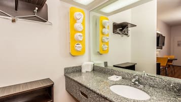 A hotel bathroom with a granite sink, a mirror, a towel rack, and a shower area.