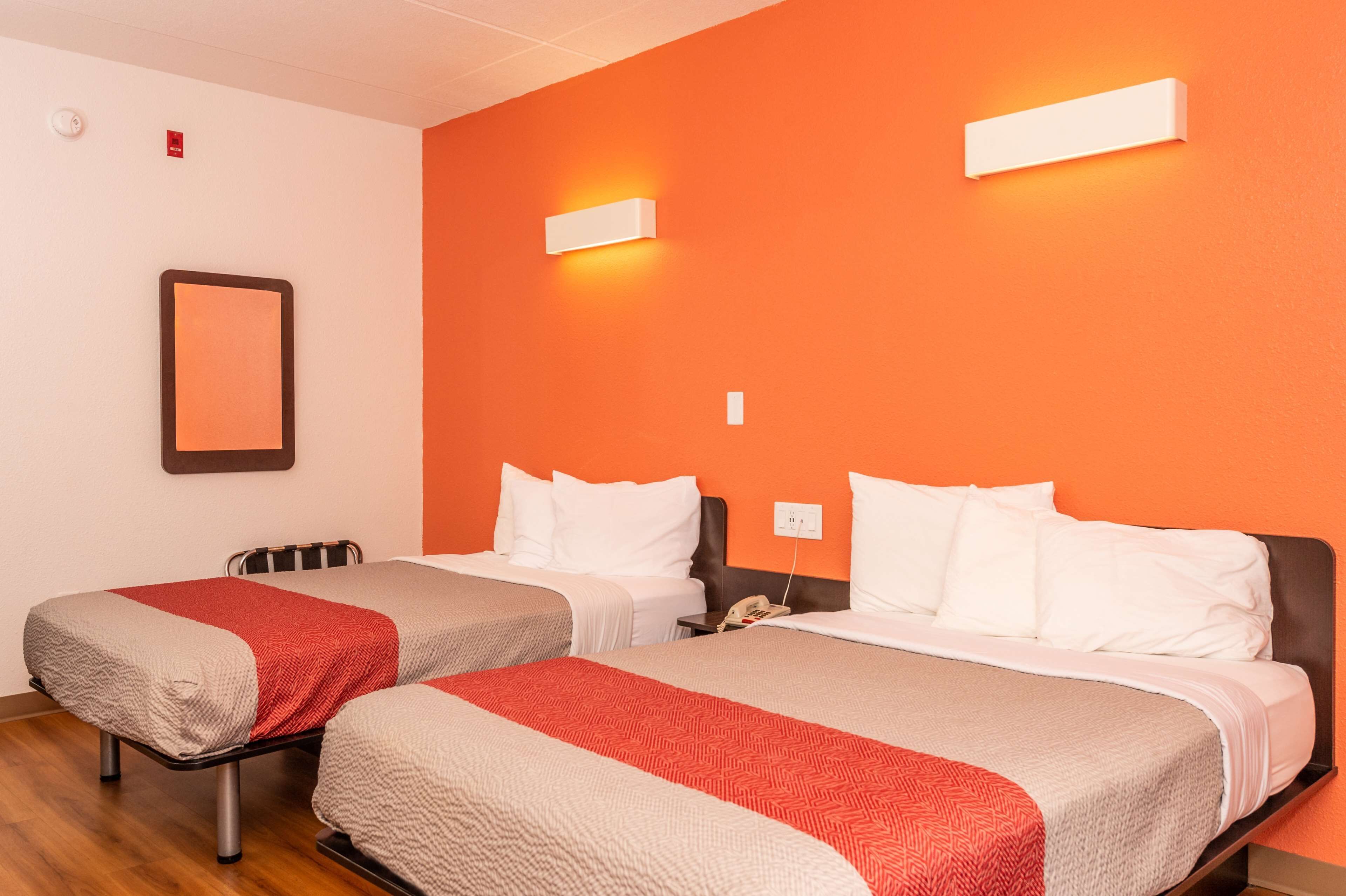 Ett hotellrum med två sängar, var och en med ett rött och beige täcke, vita kuddar och ett nattduksbord med en telefon.