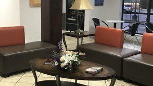En entréhall med en receptionsdisk, ett soffbord med en blomsteruppsättning och sittgrupper med orange kuddar.