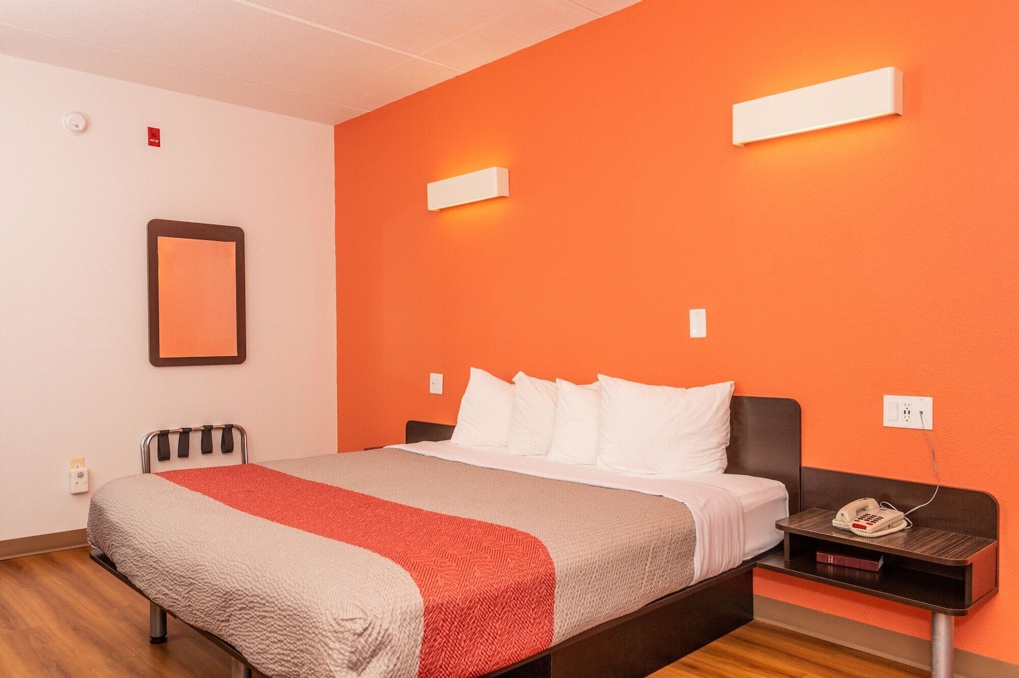 A hotel room with a bed, a nightstand, a telephone, and a mirror on the wall.