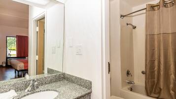 Un baño con lavamanos de encimera de granito, un espejo, una bañera y una cortina de ducha.