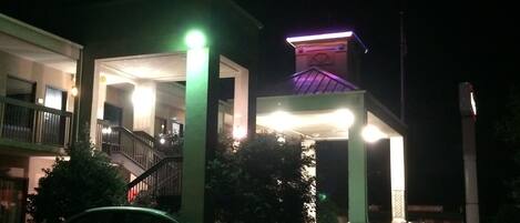 Un edificio con vestíbulo cubierto, una escalera y un coche estacionado en la entrada.