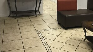 Ett väntrum med en platt-TV som visar en reklamfilm för en bil, ett konsolbord med dekorativa föremål, en röd soffa och ett klinkergolv.