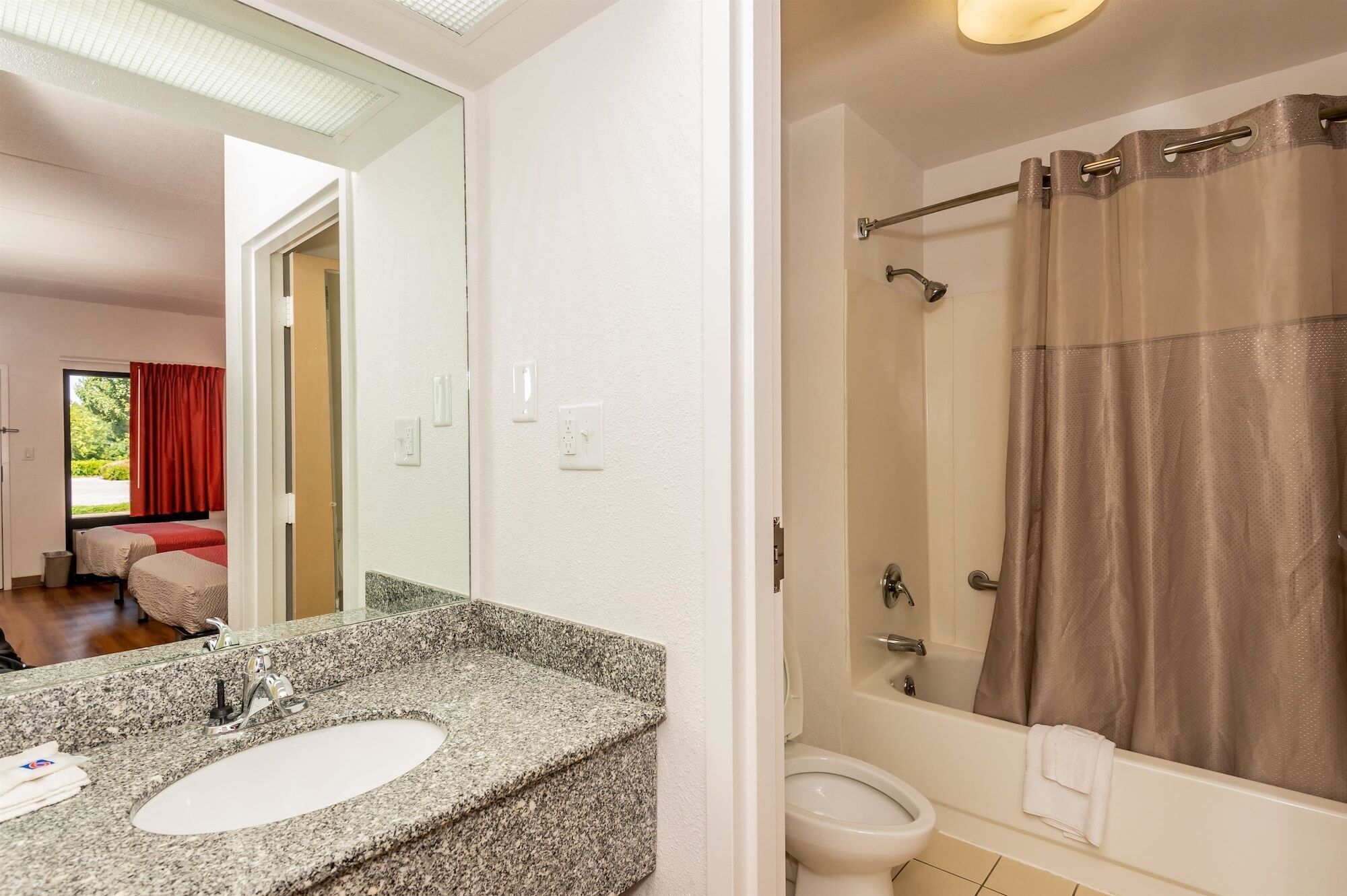 A bathroom with a granite countertop sink, a toilet, and a shower with a curtain.