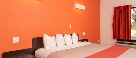 Una habitación de hotel con cama, mesitas de noche y una ventana con cortinas rojas.