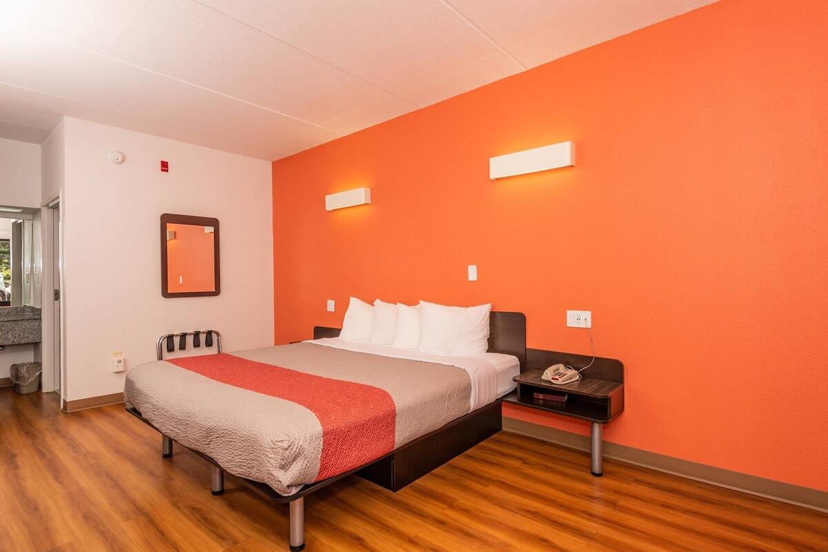 A hotel room with a bed, a nightstand, a mirror, and a red wall.
