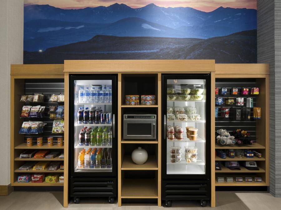 A self-service kiosk with refrigerated sections for beverages and snacks, a microwave, and a small white pot.