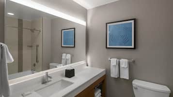 Un baño moderno con un espejo grande, lavamanos blanco y un inodoro. Se observan dos cuadros enmarcados en la pared y un perchero con toallas.