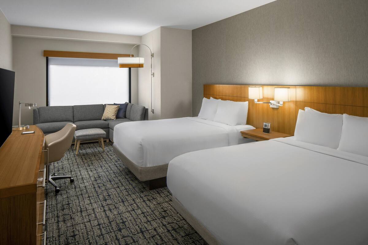 A hotel room with two beds, a desk, a sofa, and a TV.