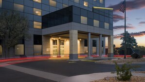 A modern building with a glass facade, a covered entrance, and an American flag. - Hyatt Place Denver/Cherry Creek (Glendale)
