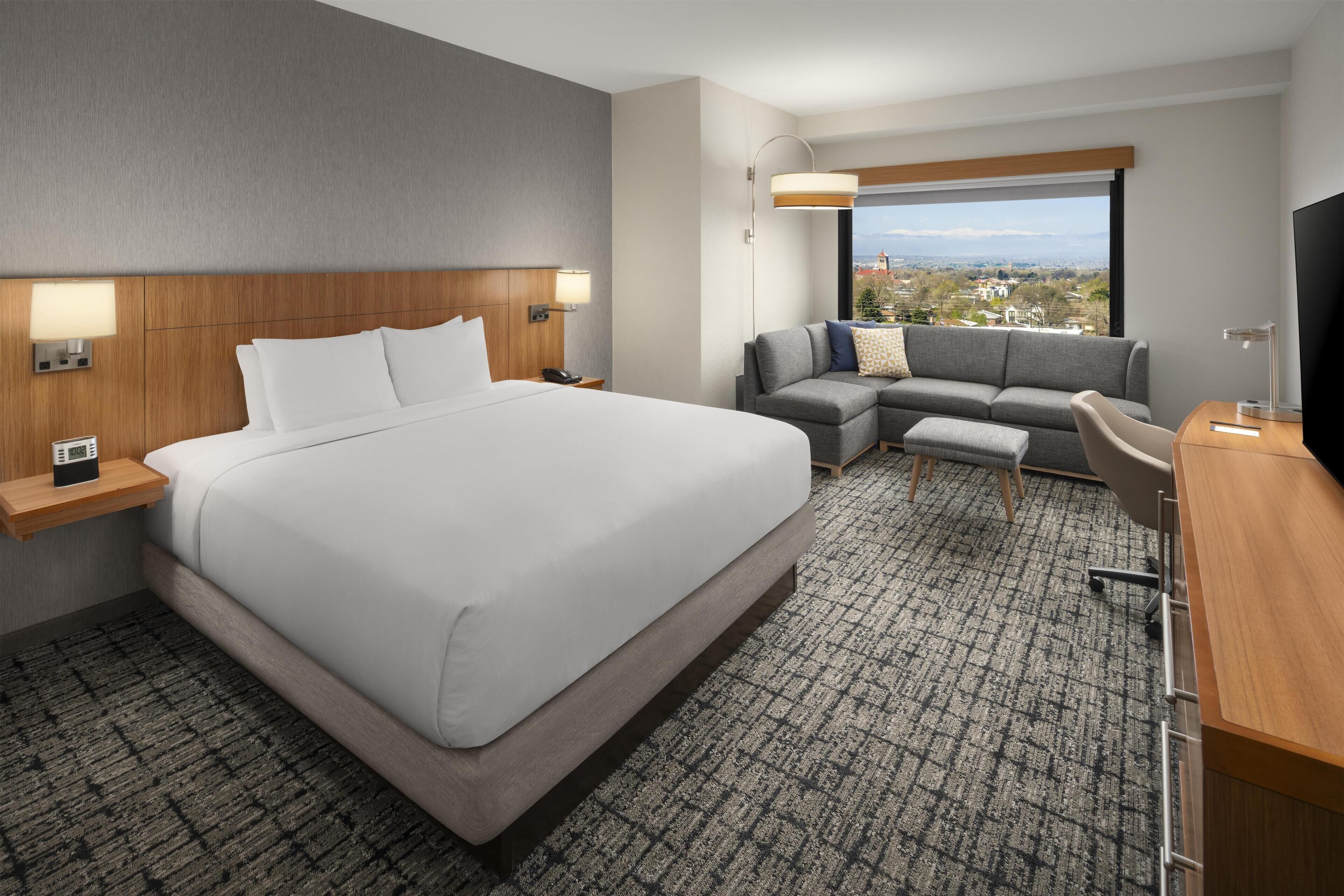 A hotel room with a large bed, a sofa, a desk, and a TV.