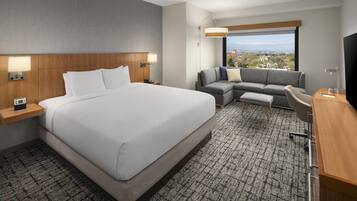 A hotel room with a large bed, a sofa, a desk, and a TV.