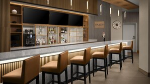 A bar area with a long counter, multiple stools, and shelves stocked with bottles and glasses. - Hyatt Place Denver/Cherry Creek (Glendale)