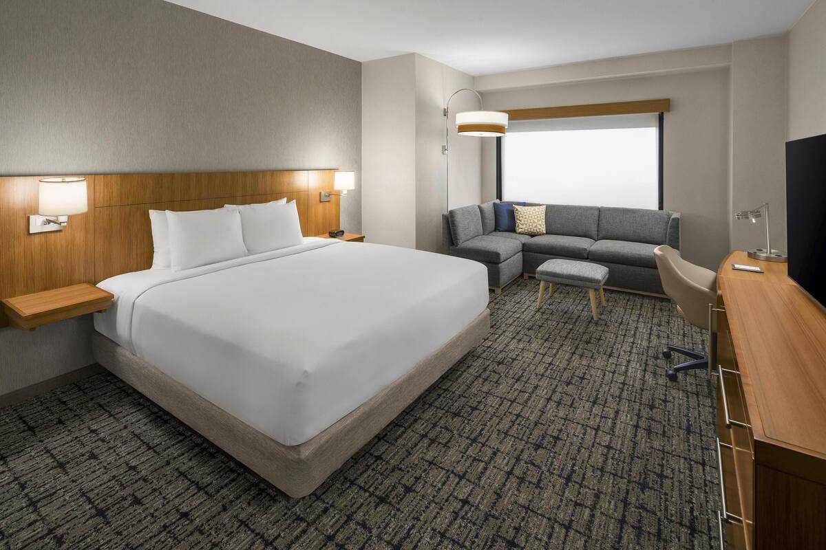 A hotel room with a large bed, a sofa, a desk, and a TV.