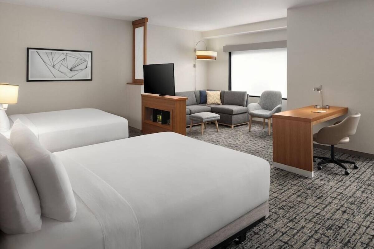 A hotel room with two beds, a TV, a desk, and a sofa.