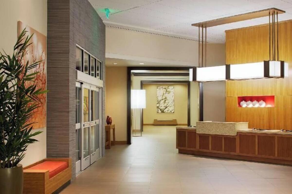 A hotel reception area with a wooden reception desk, a potted plant, and a marble wall.