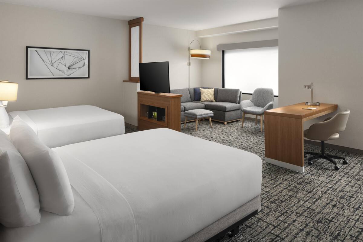 A hotel room with two beds, a TV, a desk, a chair, a lamp, and a large window.