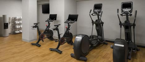 Une salle de sport équipée de divers appareils de cardio, d’un téléviseur fixé au mur et d’un porte-serviettes.