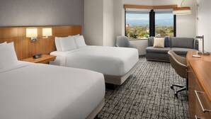 A hotel room with two beds, a desk, a chair, and a sofa. There is a large window with a view of the city and mountains. - Hyatt Place Denver/Cherry Creek (Glendale)