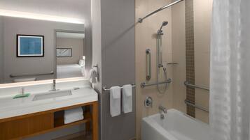 A modern bathroom with a white sink, mirror, and bathtub. There is a shower area with a glass door and a towel rack with two towels.