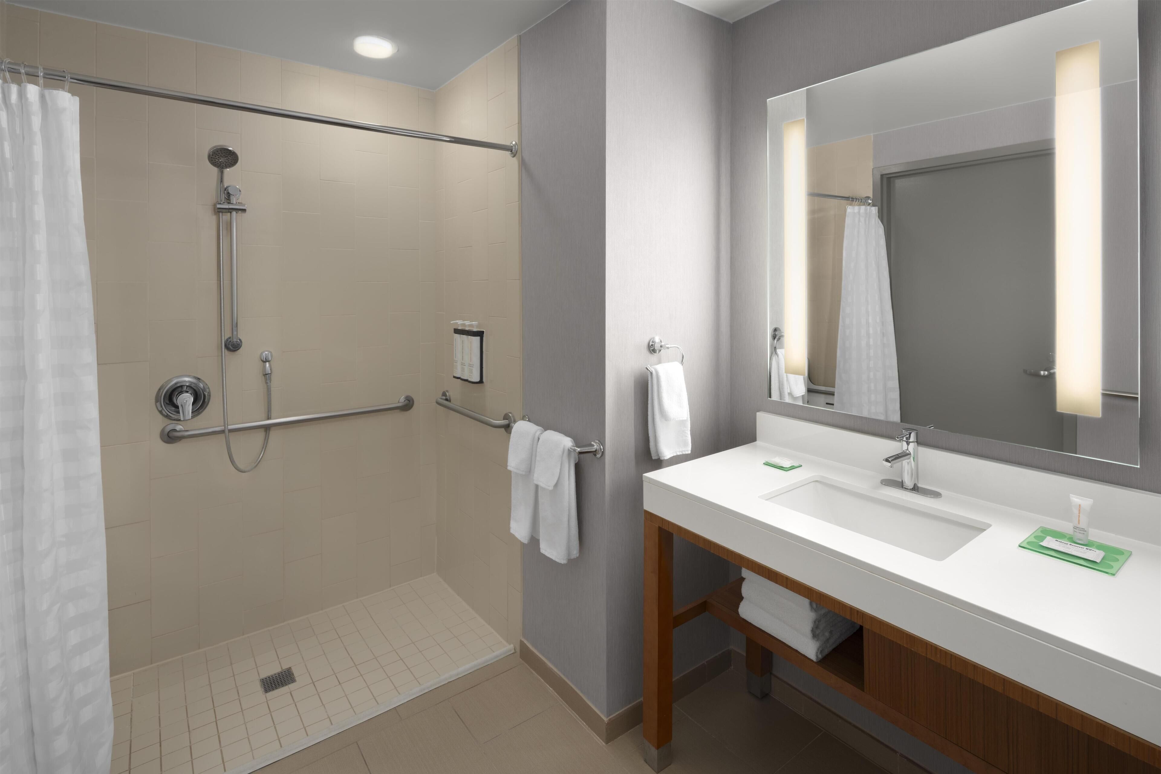 A modern bathroom with a walk-in shower, a large mirror, and a vanity with a sink and countertop.