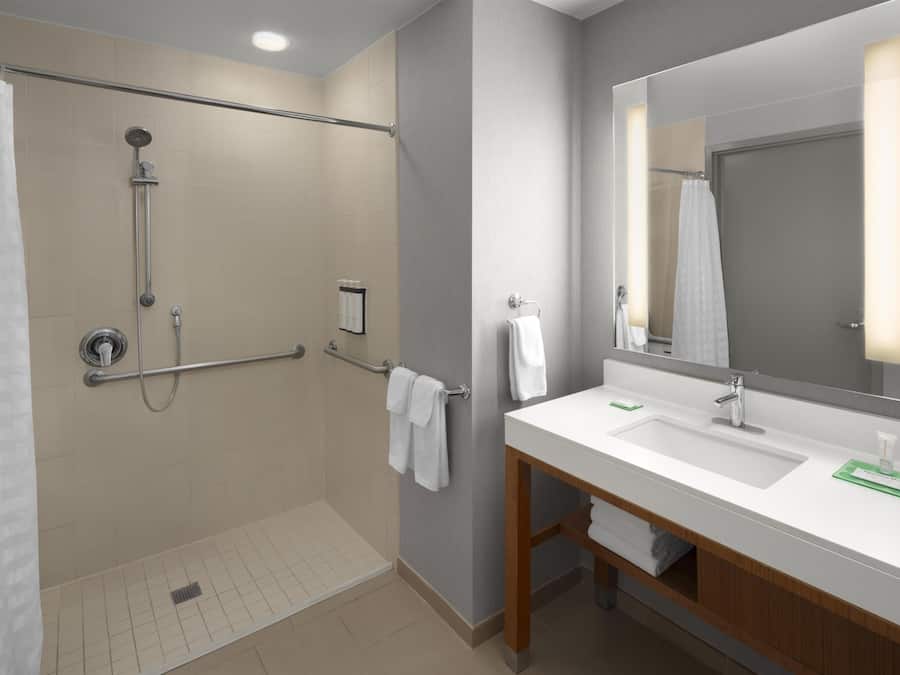 Une salle de bain moderne dotée d’une douche à l’italienne, d’un grand miroir et d’un meuble-lavabo avec un évier et un plan de travail.