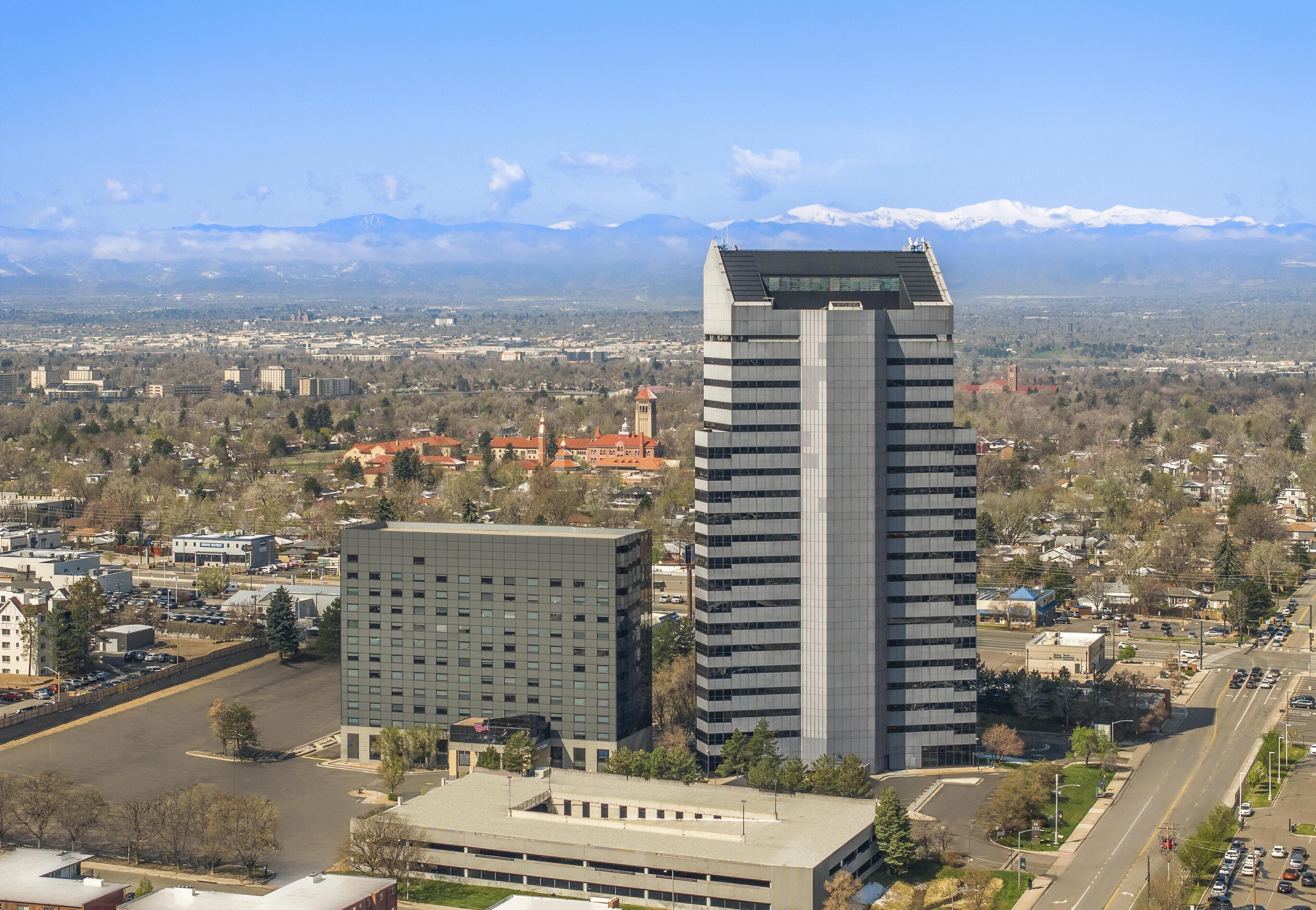 Um edifício alto com design moderno, rodeado por uma paisagem urbana e montanhas ao fundo.